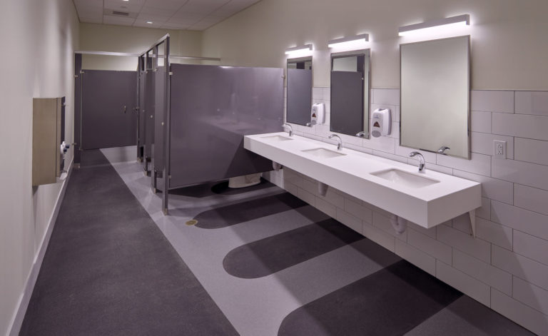 Dark grey, textured flooring marks the walkway and sinks within the bathroom.